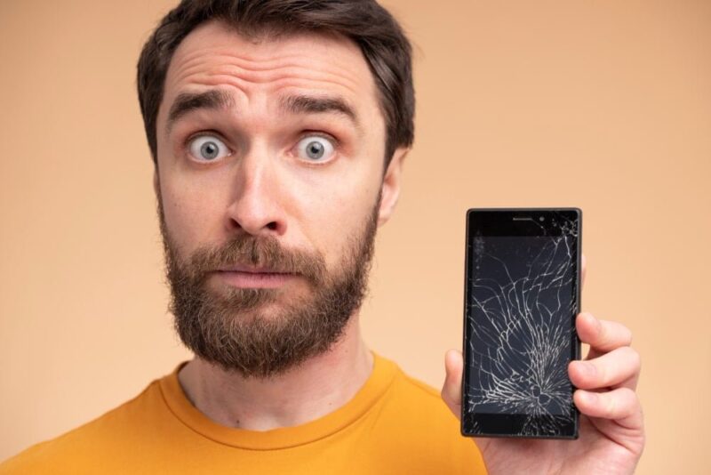 homem com celular quebrado na mão vendo o que fazer quando o celular cai no chão e não liga mais
